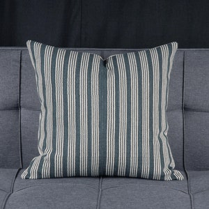 May include: A striped cushion with a dark teal and white pattern. The cushion is sitting on a grey sofa.