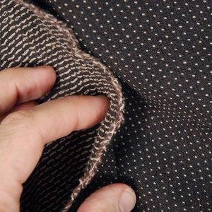 May include: Close-up of a brown fabric with a beige pattern. The fabric has a textured surface and is folded over.