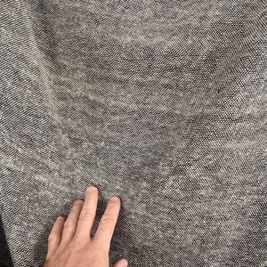 Puede incluir: Primer plano de una tela gris texturizada con una mano descansando sobre la superficie.
