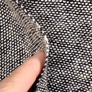 Puede incluir: Primer plano de una tela tejida en blanco y negro con un patr&oacute;n texturizado. La tela est&aacute; doblada por la mitad, revelando el tejido.