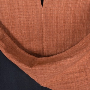 Peut inclure: Gros plan sur un tissu de couleur rouille avec un tissage textur&eacute;. Le tissu est pli&eacute; et drap&eacute;, montrant la texture et le drap&eacute; du mat&eacute;riau.