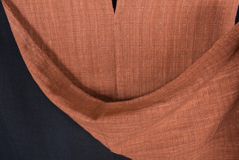 Peut inclure: Gros plan sur un tissu de couleur rouille avec un tissage textur&eacute;. Le tissu est pli&eacute; et drap&eacute;, montrant la texture et le drap&eacute; du mat&eacute;riau.