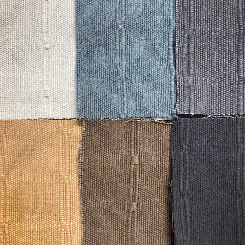 May include: A close-up of six fabric swatches in various colors. The colors include white, light blue, gray, tan, brown, and dark gray. Each swatch has a textured weave and a vertical seam down the center.