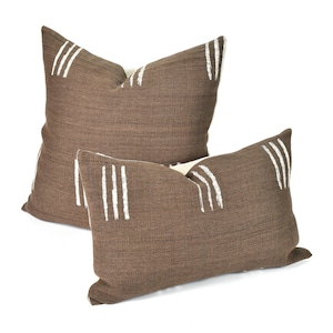 May include: Two brown throw pillows with white stripes. The pillows are made of a textured fabric and have a simple, modern design.
