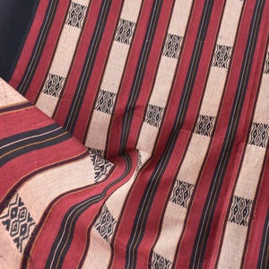 May include: Textile with a repeating pattern of vertical red, black, and cream stripes. The fabric features geometric designs in black and white. The textile is folded, showing the pattern and texture.