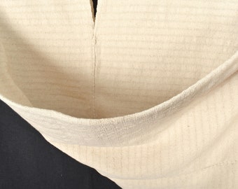 Peut inclure: Gros plan sur un sac en tissu de couleur crème avec une couture au centre. Le sac est plié en deux et le tissu est texturé.