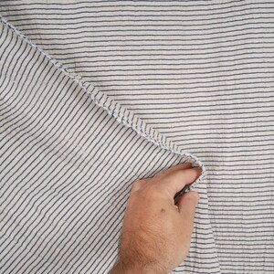 Peut inclure: Gros plan sur un tissu blanc &agrave; fines rayures bleues. Le tissu est pli&eacute; et une main tient le bord du tissu.