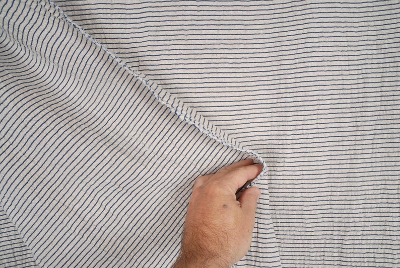 Peut inclure: Gros plan sur un tissu blanc &agrave; fines rayures bleues. Le tissu est pli&eacute; et une main tient le bord du tissu.