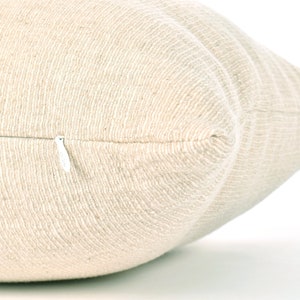 May include: Close-up of a cream-colored pillow with a zipper closure. The pillow is made of a textured fabric.