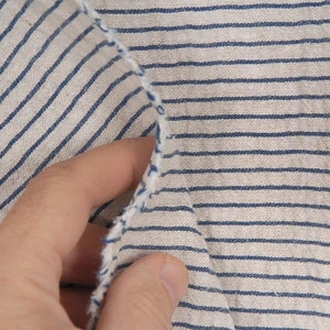 Peut inclure: Gros plan sur un tissu blanc &agrave; fines rayures bleues. Le tissu est pli&eacute; et une main le tient.