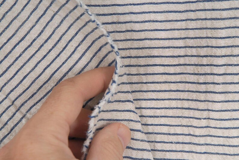 Peut inclure: Gros plan sur un tissu blanc &agrave; fines rayures bleues. Le tissu est pli&eacute; et une main le tient.