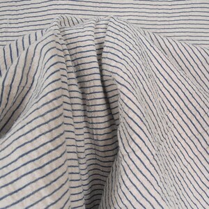 Peut inclure: Gros plan sur un tissu blanc &agrave; fines rayures bleues. Le tissu est pli&eacute; et froiss&eacute;, cr&eacute;ant un aspect textur&eacute;.