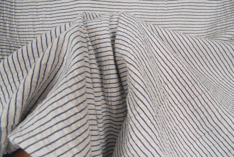 Peut inclure: Gros plan sur un tissu blanc &agrave; fines rayures bleues. Le tissu est pli&eacute; et froiss&eacute;, cr&eacute;ant un aspect textur&eacute;.