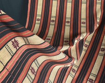 May include: Close-up of a woven fabric with a striped pattern in black, beige, and red. The fabric features geometric star and triangle designs. The material is draped, showing the texture and pattern variations.