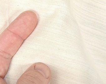 Könnte beinhalten: Nahaufnahme eines einfarbigen, gebrochenen Weißstoffes mit leicht strukturierter Oberfläche. Der Stoff ist glatt und scheint aus Naturfasern zu bestehen.