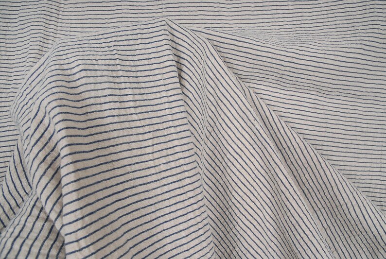 Peut inclure: Gros plan sur un tissu blanc &agrave; fines rayures bleues. Le tissu est pli&eacute; et froiss&eacute;, cr&eacute;ant un aspect textur&eacute;.
