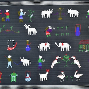 以下が含まれることがあります： 動物、人々、物体の白い刺繍が施された濃い灰色の生地。象、ヤギ、鳥、さまざまなポーズの人間の姿など、カラフルなアクセントが施されています。生地は上部と下部に白いストライプがあります。