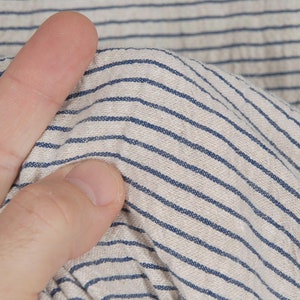 Peut inclure: Gros plan sur un tissu blanc &agrave; fines rayures bleues. Le tissu est textur&eacute; et pr&eacute;sente un aspect l&eacute;g&egrave;rement froiss&eacute;.