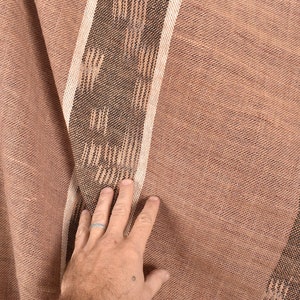 May include: A close-up of a brown woven fabric with a white and brown striped pattern. The fabric has a textured surface and is folded in the center.