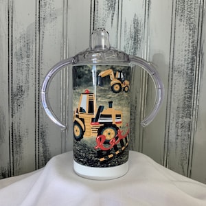 May include: A clear plastic sippy cup with two handles and a yellow and black construction vehicle design. The cup has a white lid with a clear spout.