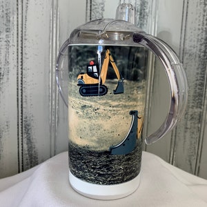 May include: A white stainless steel tumbler with a clear plastic lid and two handles. The tumbler has a printed image of a yellow toy excavator on a dirt background.
