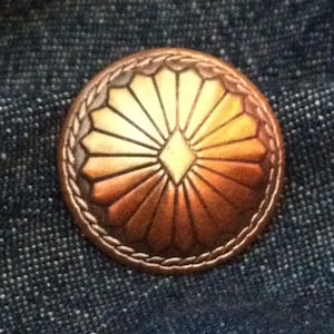 May include: A copper-colored button with a raised, sunburst design and a diamond in the center. The button has a rope-like border.