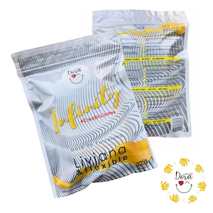 May include: A white bag with a yellow and black striped design. The bag contains a white and yellow package of air-dry clay. The package has the text "Infinity #CreaSinLímites Masa de Porcelana Liviana & flexible 325g" on it. The bag also has a sticker with a red heart and the text "Dera" on it.