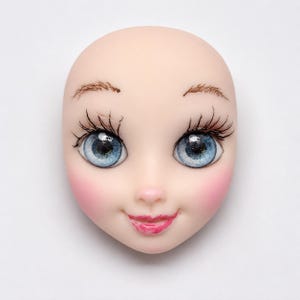 May include: A doll face with a smooth, pale complexion. The face features large, detailed blue eyes with long black eyelashes, delicate brown eyebrows, and rosy cheeks. The lips are painted a bright pink, and the face has a slight smile.