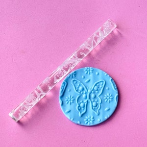 May include: A clear acrylic rolling pin with a butterfly and floral design, and a blue silicone rolling pin with a butterfly design.