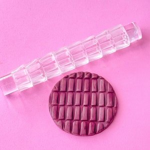 May include: A clear acrylic rolling pin with a textured pattern and a dark purple fondant circle with the same pattern.
