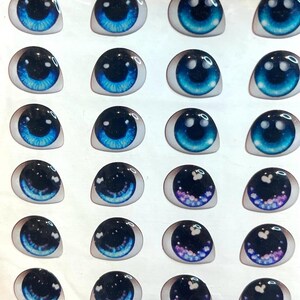 May include: A sheet of 20 blue, black, and purple doll eyes with a white background. The eyes have different designs, including stars, swirls, and glitter. The sheet is labeled "Art 220 A Super".