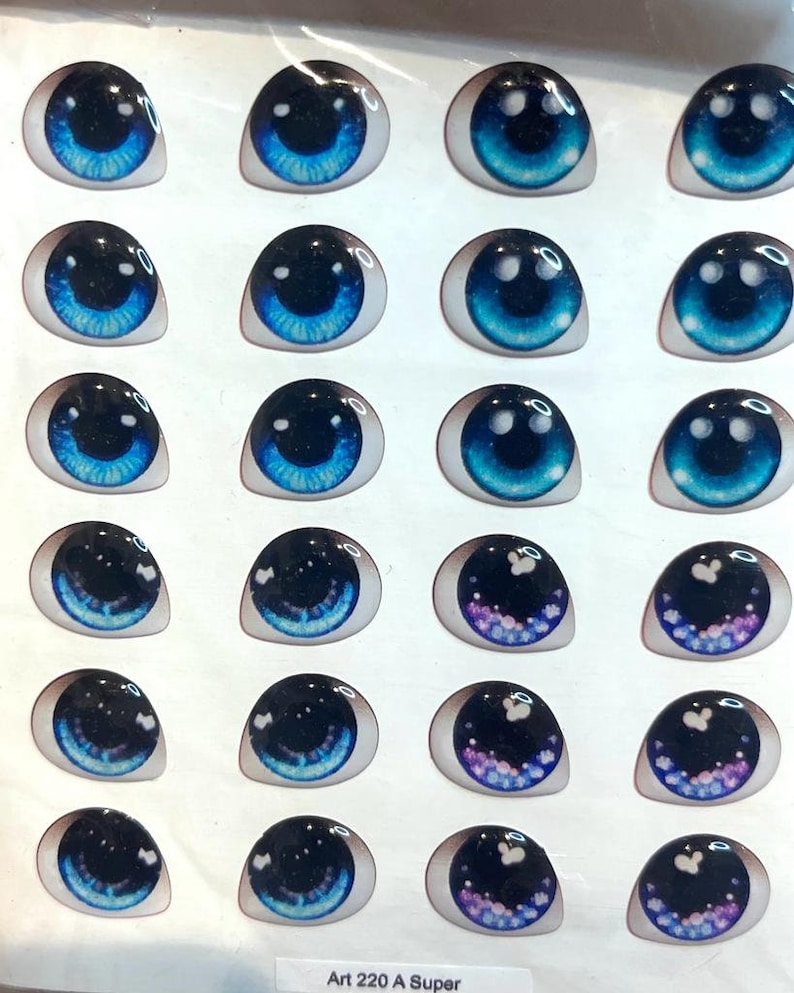 May include: A sheet of 20 blue, black, and purple doll eyes with a white background. The eyes have different designs, including stars, swirls, and glitter. The sheet is labeled "Art 220 A Super".