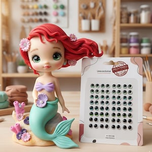 Può includere: Una statuetta di sirena con capelli rossi, occhi verdi e coda color verde acqua, seduta su una base con corallo rosa e fiori, accanto a una confezione di occhi artigianali da 6mm verdi e neri etichettata Erica Perrez Linea exclusiva Art 035-6 MM.