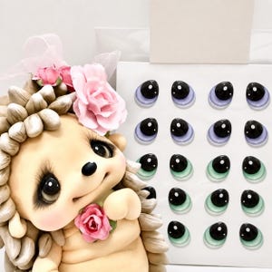 May include: A whimsical, handcrafted hedgehog figurine with a light tan body, adorned with a pink flower and a matching bow. Beside it, a collection of miniature, detailed eye sets in various shades of blue and green.