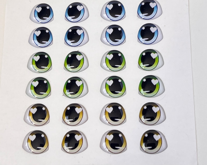 May include: A sheet of 24 plastic doll eyes with a heart design. The eyes are in various colors, including blue, green, and brown.