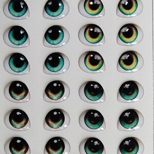 May include: A sheet of 20 doll eyes, with a variety of colors and designs. The eyes are arranged in four rows of five. The eyes are all oval shaped and have a black pupil. The colors of the eyes include green, brown, and yellow. The sheet is labeled "Art 220 Super".