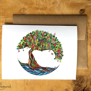 May include: A colorful greeting card featuring a hand-drawn illustration of a tree of life with green leaves, pink flowers, and a blue and purple water-like base. The tree is surrounded by a circle and has birds flying around it.