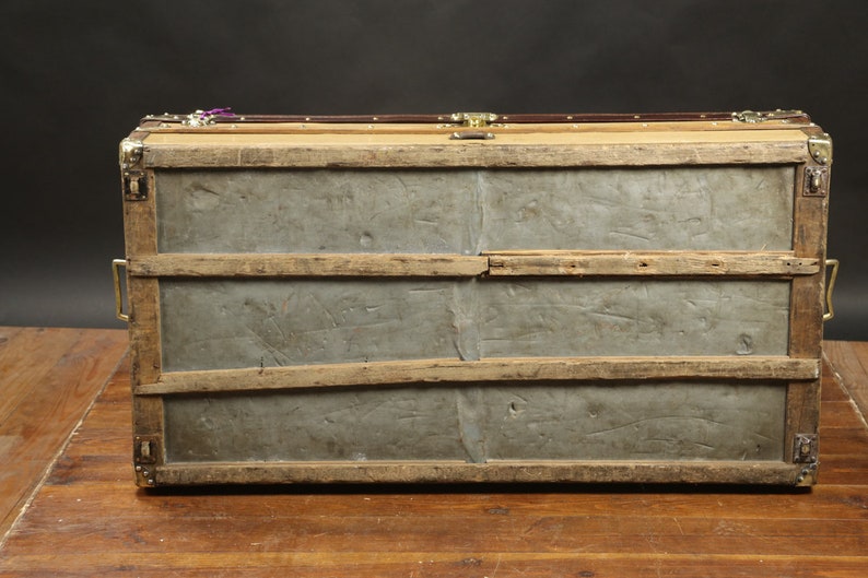 May include: A vintage wooden trunk with metal accents and a metal bottom. The trunk has a worn, distressed look and is secured with brass clasps.