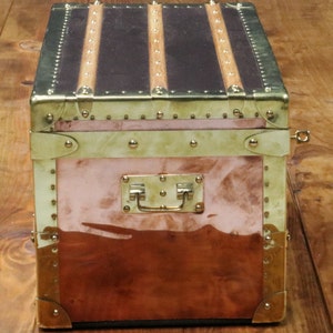 May include: A vintage copper and brass travel trunk with a leather top and brass hardware. The trunk has a brass handle and a brass lock.