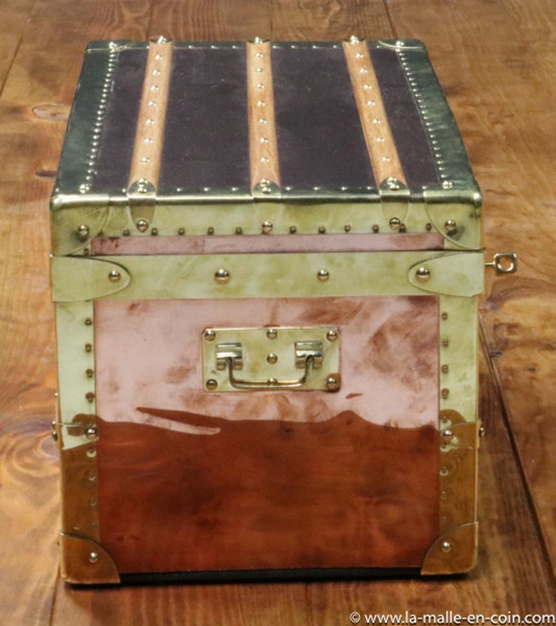 May include: A vintage copper and brass travel trunk with a leather top and brass hardware. The trunk has a brass handle and a brass lock.