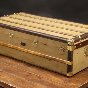 May include: A vintage canvas and leather travel trunk with brass hardware and a wooden frame. The trunk has a worn, distressed look and is a great piece for home decor.