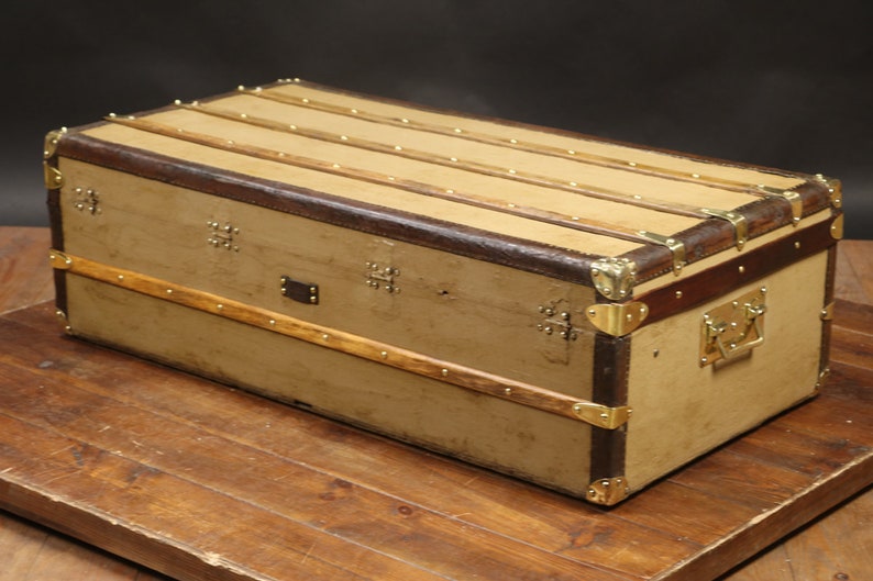 May include: A vintage canvas and leather travel trunk with brass hardware and a wooden frame. The trunk has a worn, distressed look and is a great piece for home decor.