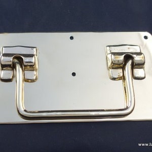 May include: A gold-toned metal handle with a rectangular plate and a curved, D-shaped handle. The handle is attached to the plate with two decorative pieces on each side.