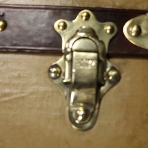 May include: Close-up of a brass latch with a star-shaped design and five decorative rivets. The latch is closed and has a small, rectangular metal plate with the word "Genuine" engraved on it.