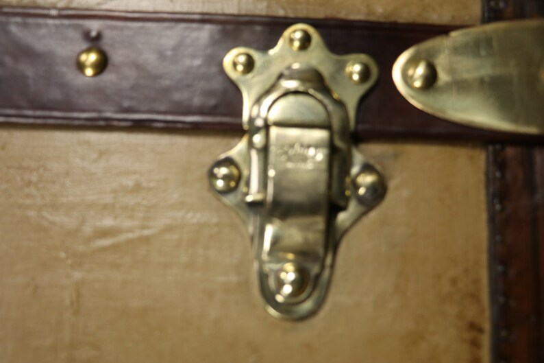 May include: Close-up of a brass latch with a star-shaped design and five decorative rivets. The latch is closed and has a small, rectangular metal plate with the word "Genuine" engraved on it.