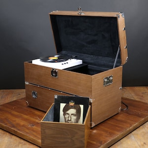 May include: A wooden record player in the shape of a vintage suitcase with a record on the turntable. The suitcase is open and the turntable is visible. There is a record album in the bottom compartment of the suitcase.