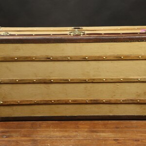 May include: A vintage brown leather-trimmed canvas luggage trunk with brass hardware and wooden straps.