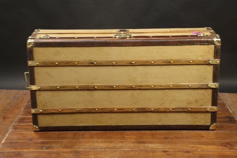 May include: A vintage brown leather-trimmed canvas luggage trunk with brass hardware and wooden straps.