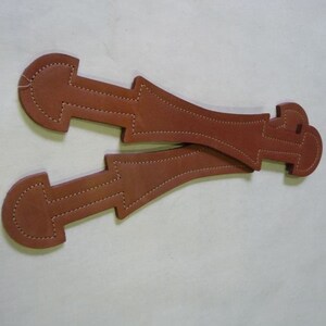 May include: Two brown leather straps with stitching, each with a loop at one end and a pointed end at the other.