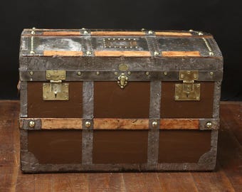 May include: A vintage brown leather and metal travel trunk with brass hardware and a lock. The trunk has a rectangular shape and is decorated with metal bands and studs.